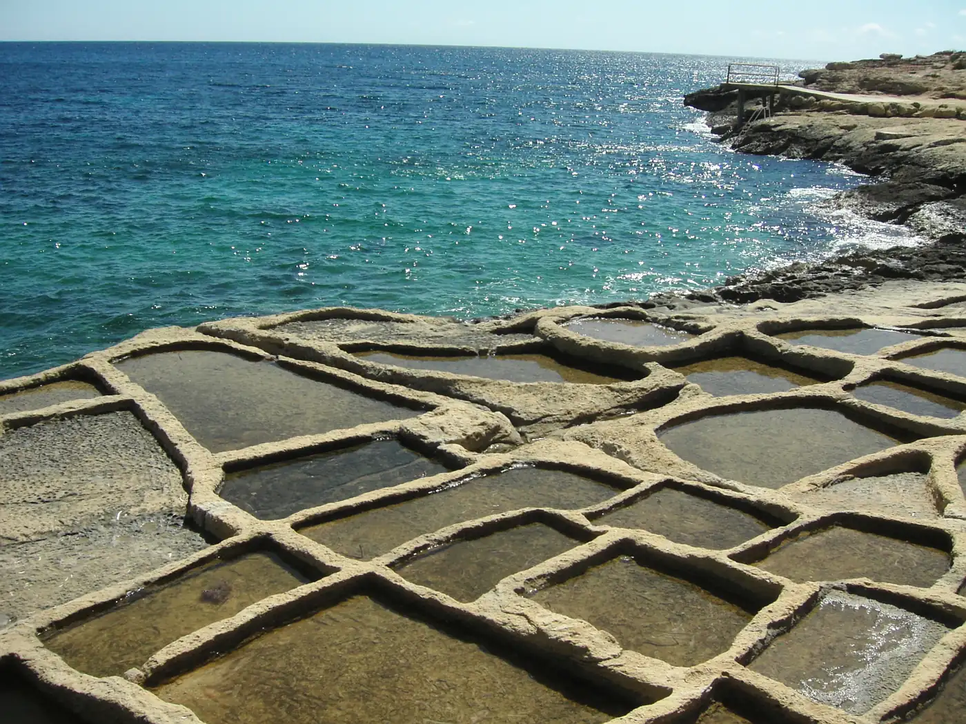 Old rock-cut salt pans on the coast of Gozo with the turquoise sea behind
